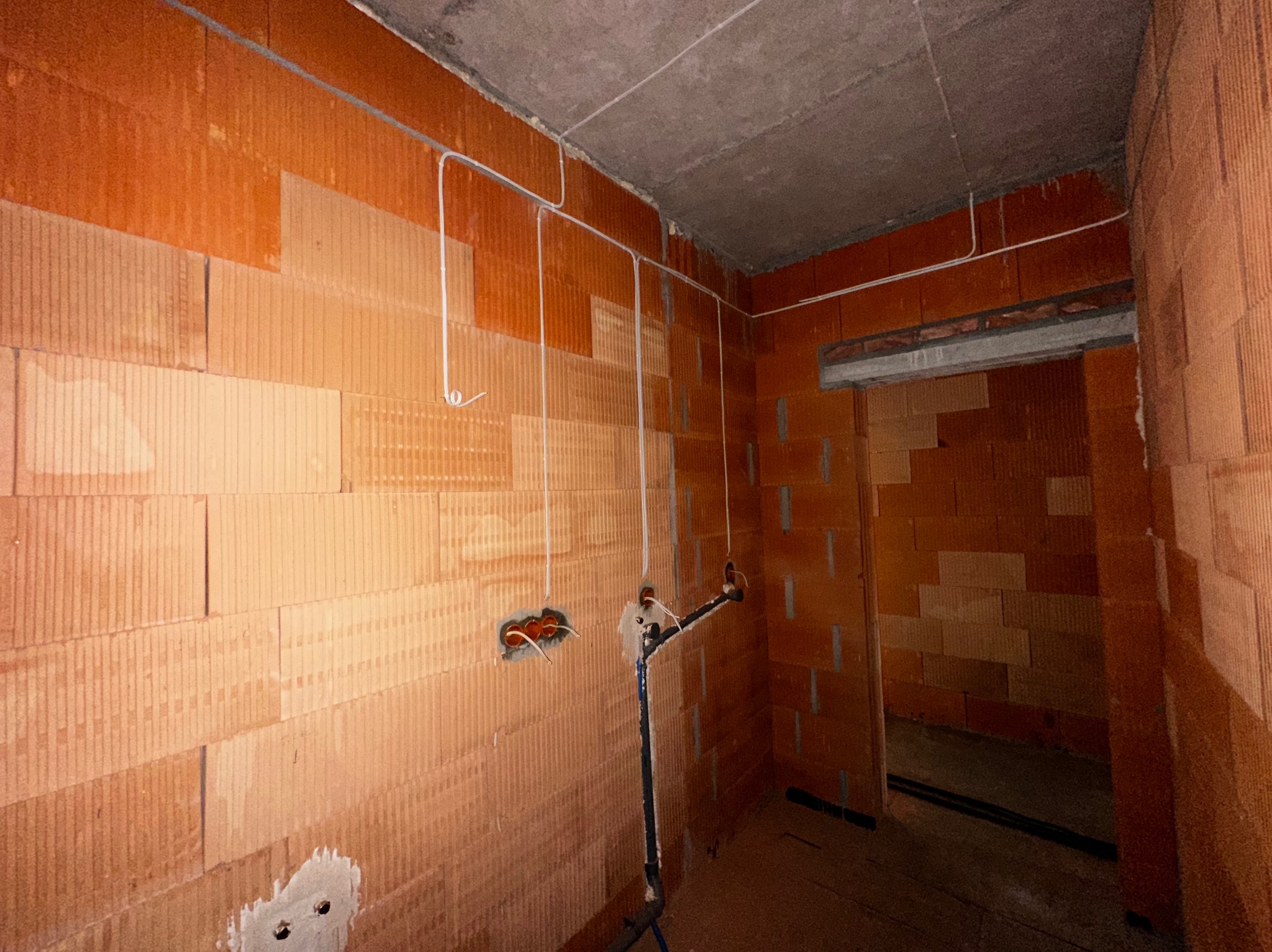 Wnętrze w trakcie prac instalacyjnych: widoczne przewody elektryczne poprowadzone po ścianach z pustaków ceramicznych, puszki elektryczne przygotowane do montażu gniazdek.