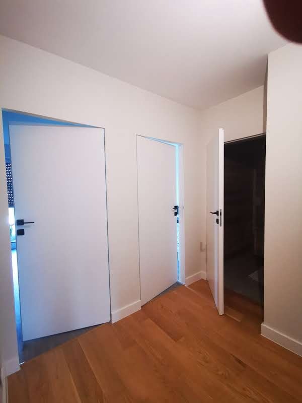 Nowoczesne, minimalistyczne wnętrze z trzema białymi, bezprzylgowymi drzwiami i parkietem ułożonym w jodełkę.