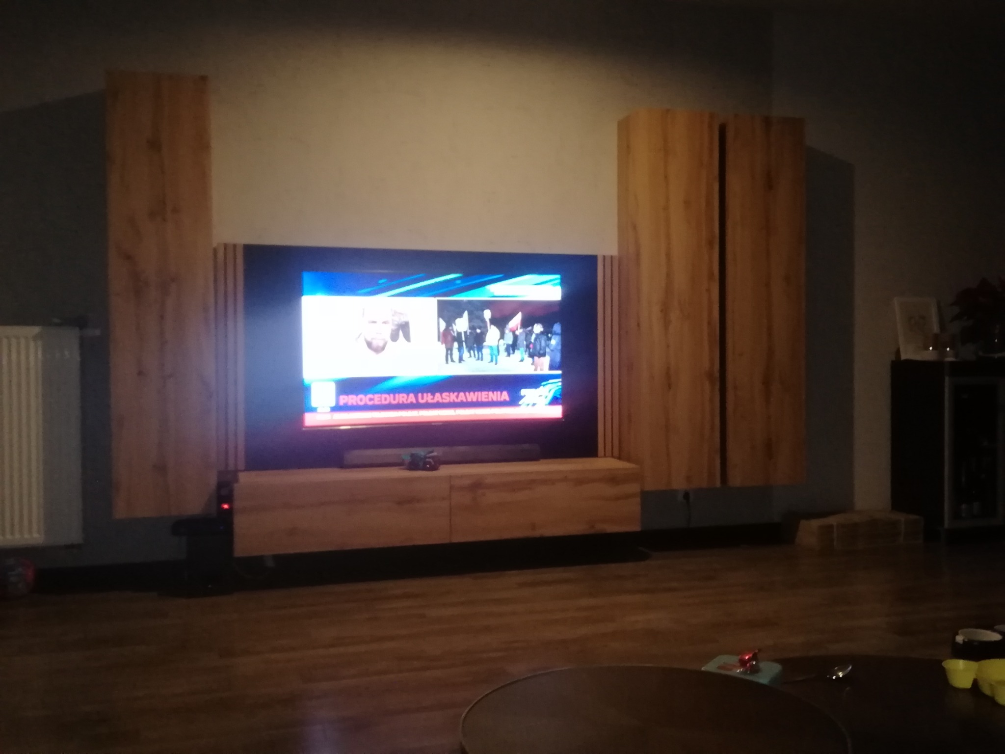 Nowoczesna meblościanka w odcieniach drewna z szafką RTV pod telewizorem, widok z dołu w słabym oświetleniu.