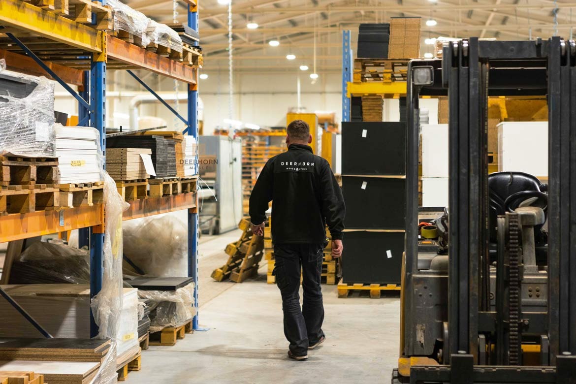 Magazyn z półkami pełnymi blatów drewnianych i płyt meblowych, w tle pracownik firmy Deerhorn.