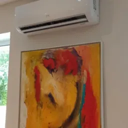 Biały klimatyzator ścienny marki CH, zamontowany nad abstrakcyjnym obrazem w salonie. Na wyświetlaczu klimatyzatora widoczna temperatura 16 stopni.