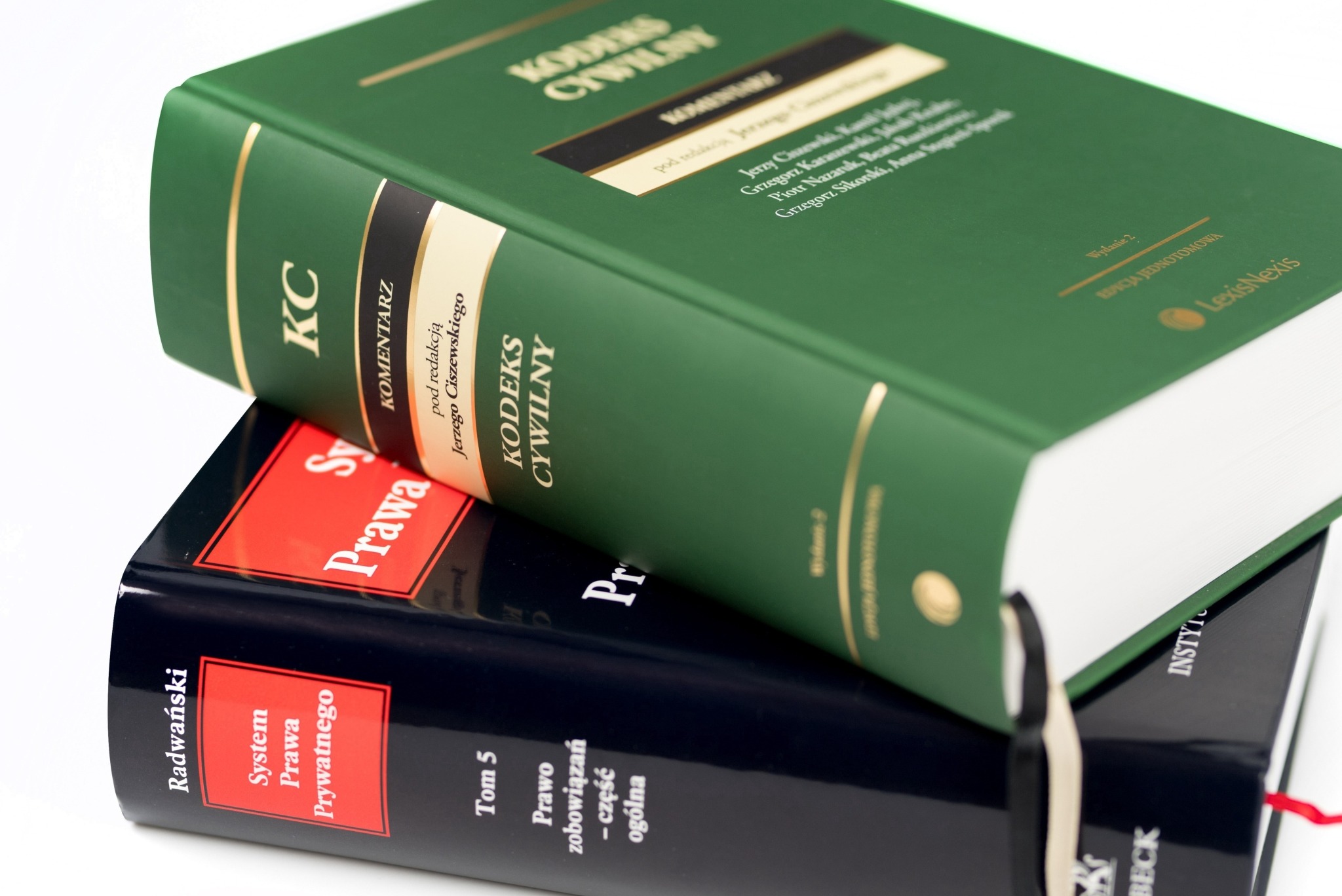 Stos kodeksów prawnych: zielony tom 'Kodeks Cywilny' na czarnym tomie 'System Prawa Prywatnego', z widocznymi złotymi napisami i zakładkami.