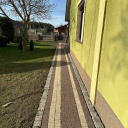 MYCIE WYSOKOCIŚNIENIOWE KAJETAN KULUS - Ułożona ścieżka z kostki brukowej w dwóch kolorach, prowadząca wzdłuż ściany domu o żółtej elewacji, widok z perspektywy niskiego kąta.