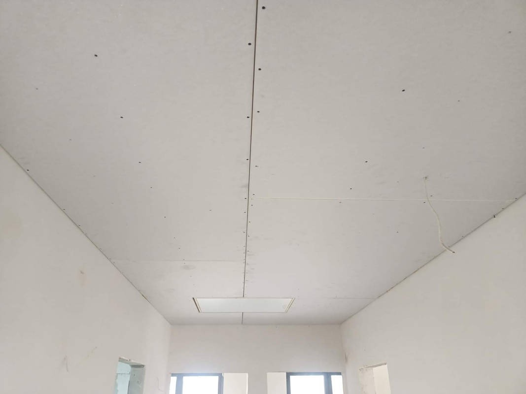 Montaż płyt gipsowo-kartonowych na suficie, widoczne łączenia płyt i otwór rewizyjny, surowe ściany w tle.