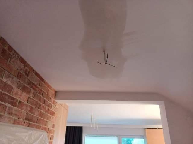 Niedokończone malowanie sufitu w Łowiczu, widoczne ślady po zalaniu i wystające kable, ceglana ściana w tle.