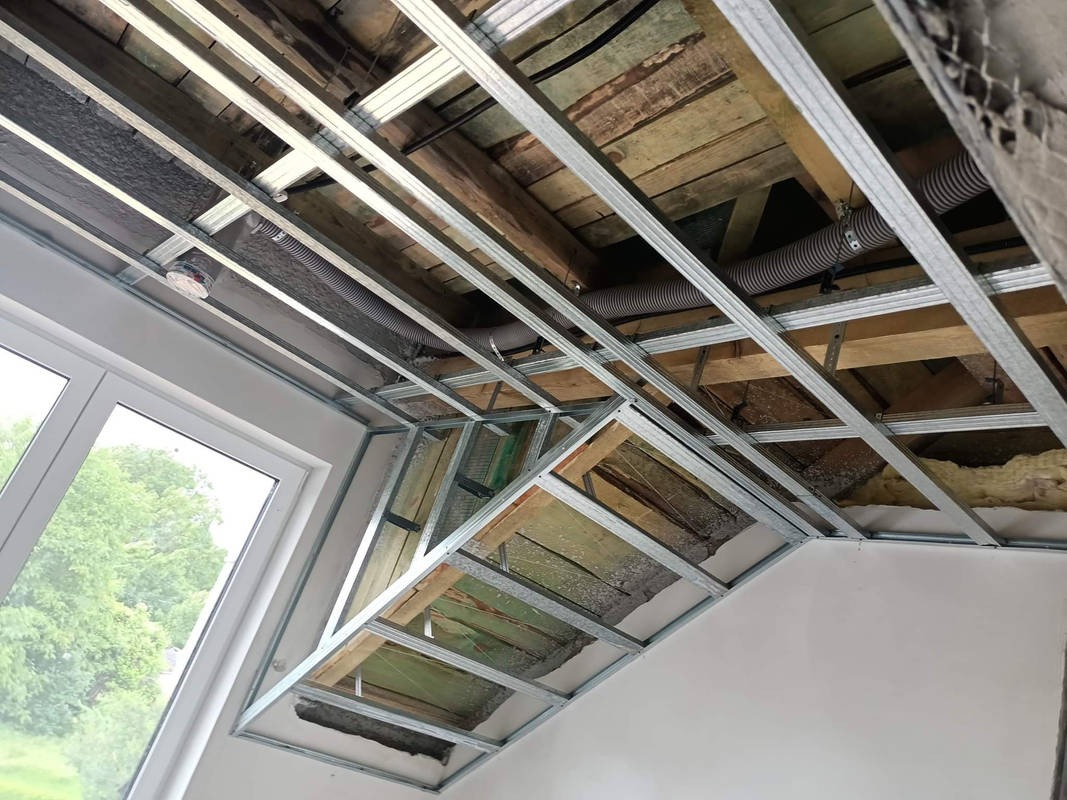 Montaż sufitu podwieszanego z metalowej konstrukcji na poddaszu, widoczne ocieplenie, elementy wentylacji i okno dachowe.