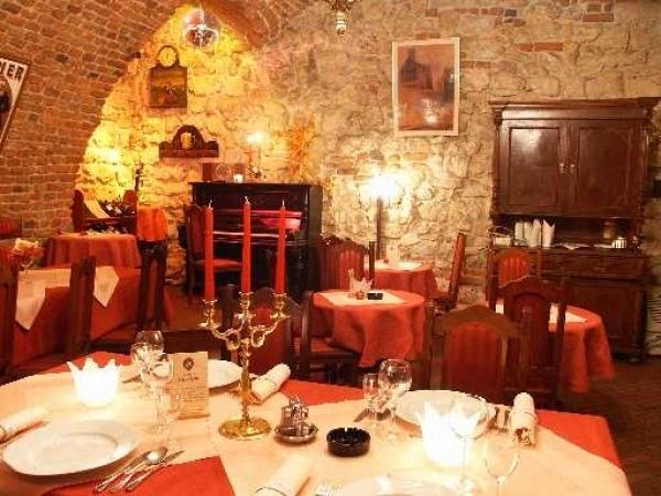 Uroczysta aranżacja stołu w klimatycznej sali restauracyjnej z kamiennymi ścianami, świecami, pianinem w tle i dekoracyjnym oświetleniem tworząca intymną atmosferę.