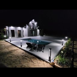 Pomorskie Tarasy - Nowoczesny dom z basenem oświetlonym nocą. Dwa leżaki przy basenie. Oświetlenie ścieżki lampami. Minimalistyczny design domu z dużymi oknami i oświetleniem zewnętrznym.