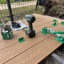Pomorskie Tarasy - Montaż desek tarasowych: wkrętarka Makita, klipsy montażowe Spax, narzędzie do dociskania desek na brązowym tarasie. Widoczne elementy konstrukcji nośnej.