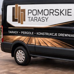 Pomorskie Tarasy - Czarny van z logo firmy 'Pomorskie Tarasy' oferującej tarasy, pergole i konstrukcje drewniane, zaparkowany na brukowanym podjeździe.