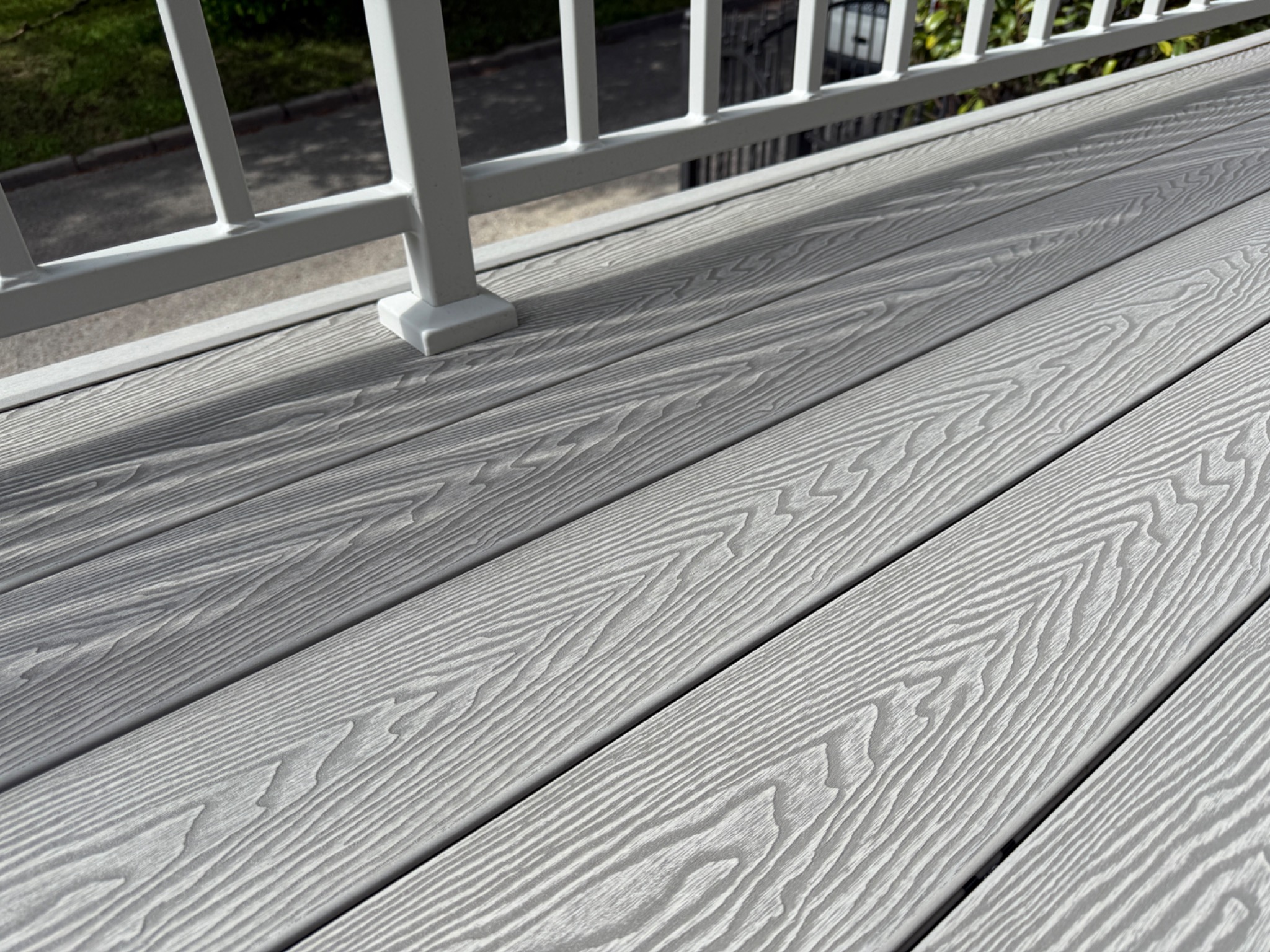 Jasnoszary taras kompozytowy z białymi barierkami, ukazujący teksturę desek i solidne wykonanie. Widok z góry, podkreślający estetykę i trwałość materiałów.