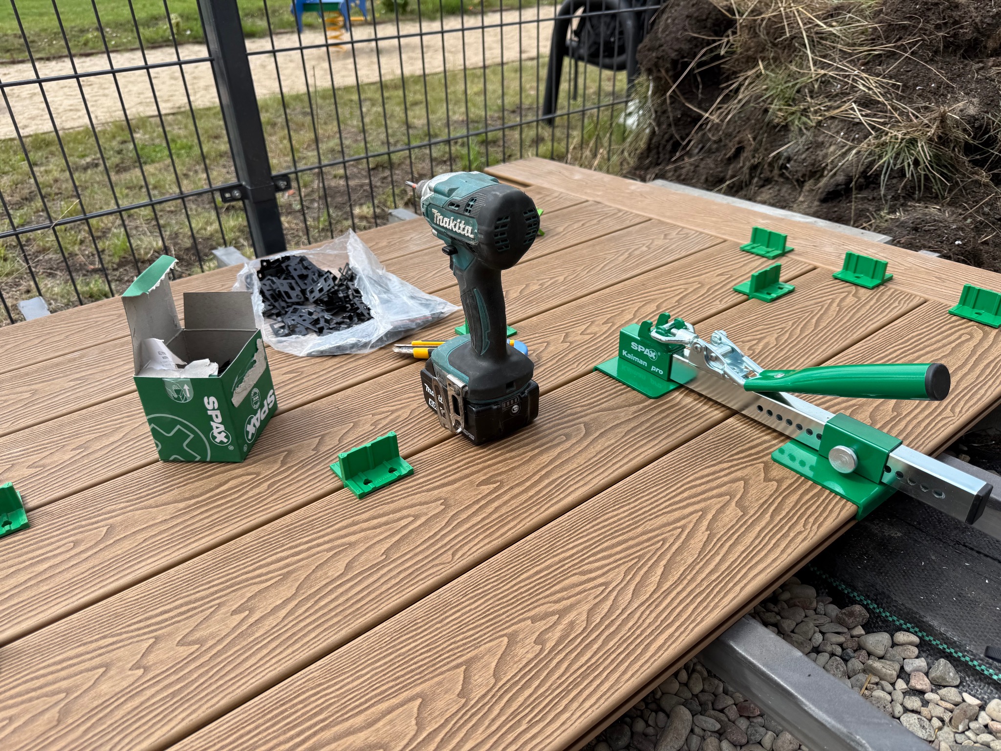 Montaż desek tarasowych: wkrętarka Makita, klipsy montażowe Spax, narzędzie do dociskania desek na brązowym tarasie. Widoczne elementy konstrukcji nośnej.