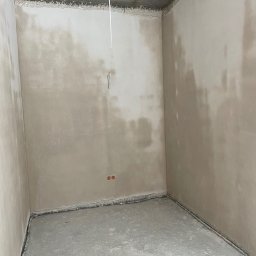 Portal-tech - Surowe wnętrze pokoju po tynkowaniu ścian i wylewce podłogi. Widoczne wystające kable i surowy betonowy strop. Ściany w odcieniach beżu.