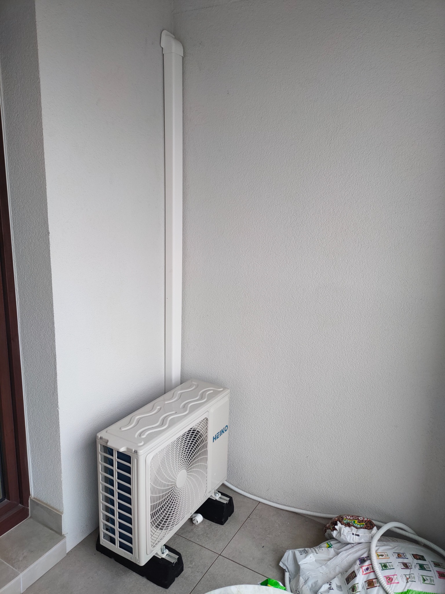 Zewnętrzna jednostka klimatyzacji Heiko zamontowana na balkonie, widoczne rury odprowadzające i maskownica na ścianie.