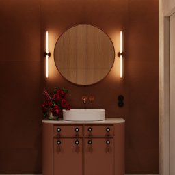 Jacek Gonera - Studio Projektowania Architektury Wnętrz - Nowoczesna łazienka w odcieniach terakoty z okrągłym lustrem podświetlonym listwami LED, umywalką nablatową i kwiatami w wazonie.