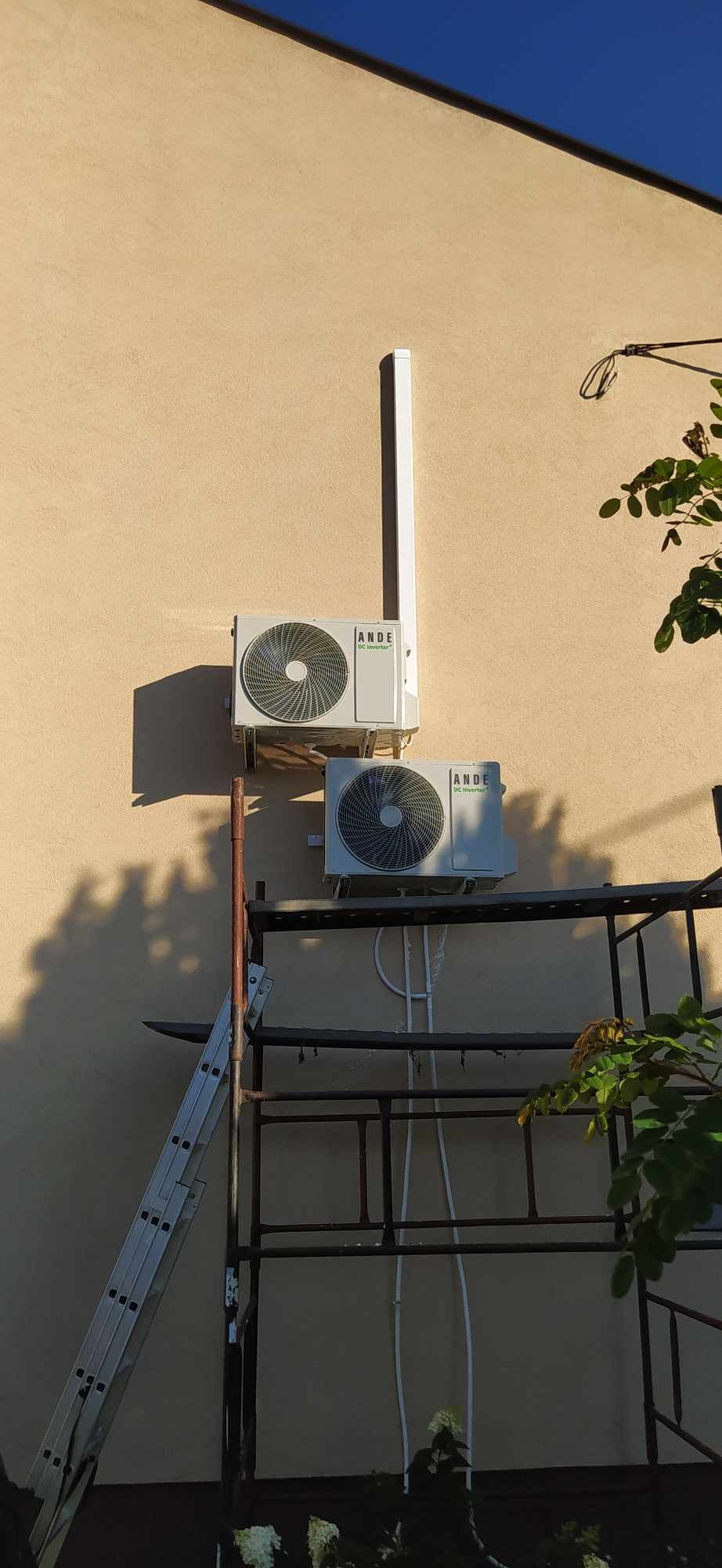 Dwa klimatyzatory marki ANDE zamontowane na beżowej ścianie budynku, widoczne rusztowanie i drabina, sugerujące trwający montaż.