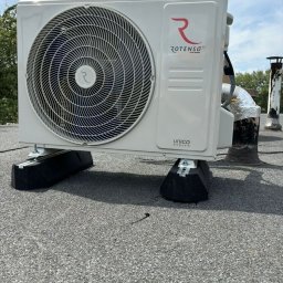 Pro Installer - Biała jednostka zewnętrzna klimatyzacji Rotenso Unico, zamontowana na dachu z papy, z widocznym kominem w tle i błękitnym niebem.