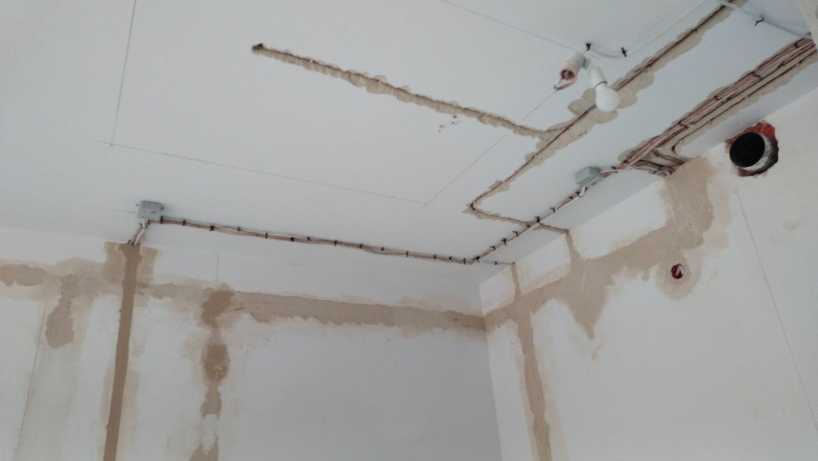 Fragment wnętrza w trakcie prac remontowych: widoczne przewody elektryczne prowadzone po ścianach i suficie, przygotowane podłoże pod tynkowanie, zarys sufitu podwieszanego.