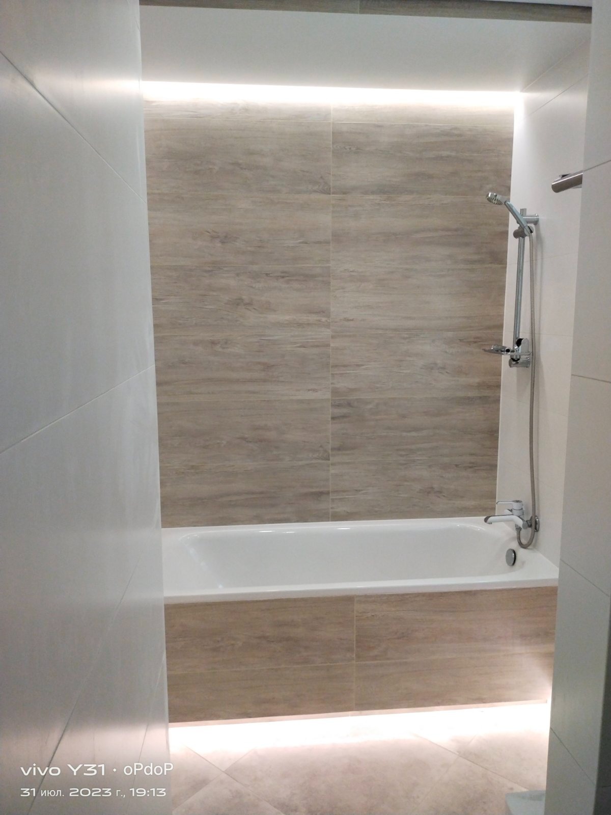 Nowoczesna łazienka z wanną obudowaną płytkami imitującymi drewno, oświetleniem LED pod sufitem i pod wanną, oraz chromowaną armaturą.