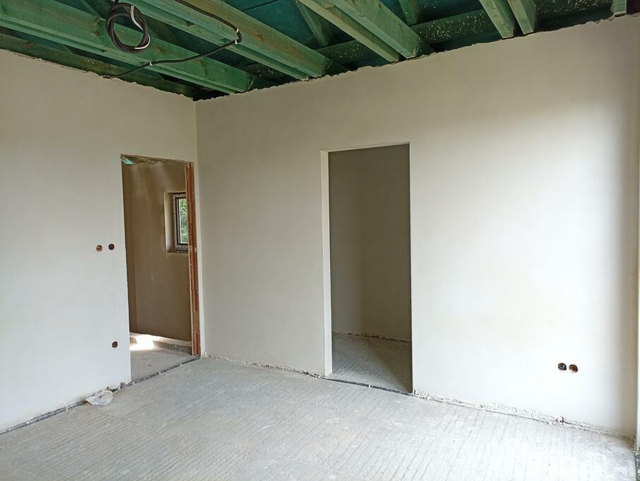 Wnętrze po nałożeniu gładzi gipsowej na ścianach, widoczne otwory na gniazdka elektryczne i surowy strop z belek pomalowanych na zielono.