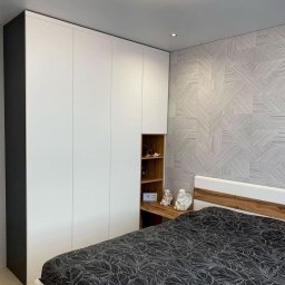 Wawrzyniak Karol - Nowoczesna sypialnia z białą szafą w zabudowie, fragmentem otwartych półek z drewnianym wykończeniem i dekoracyjną tapetą w geometryczne wzory.