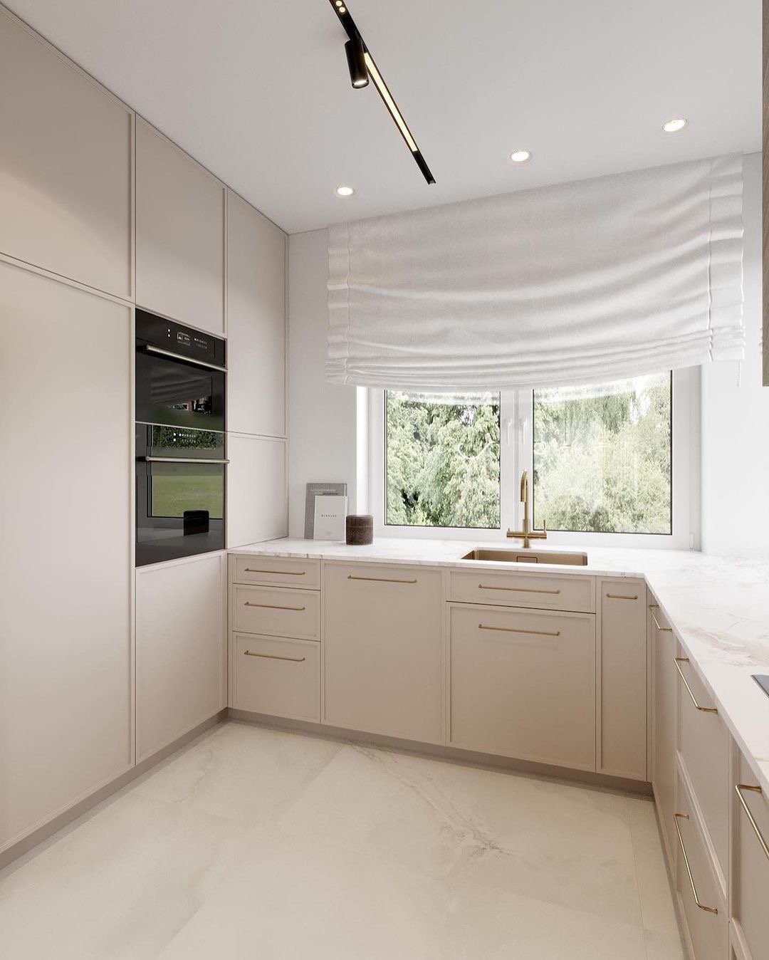 Jasna kuchnia z beżowymi frontami szafek, złotymi uchwytami, marmurowym blatem i widokiem na zieleń za oknem.