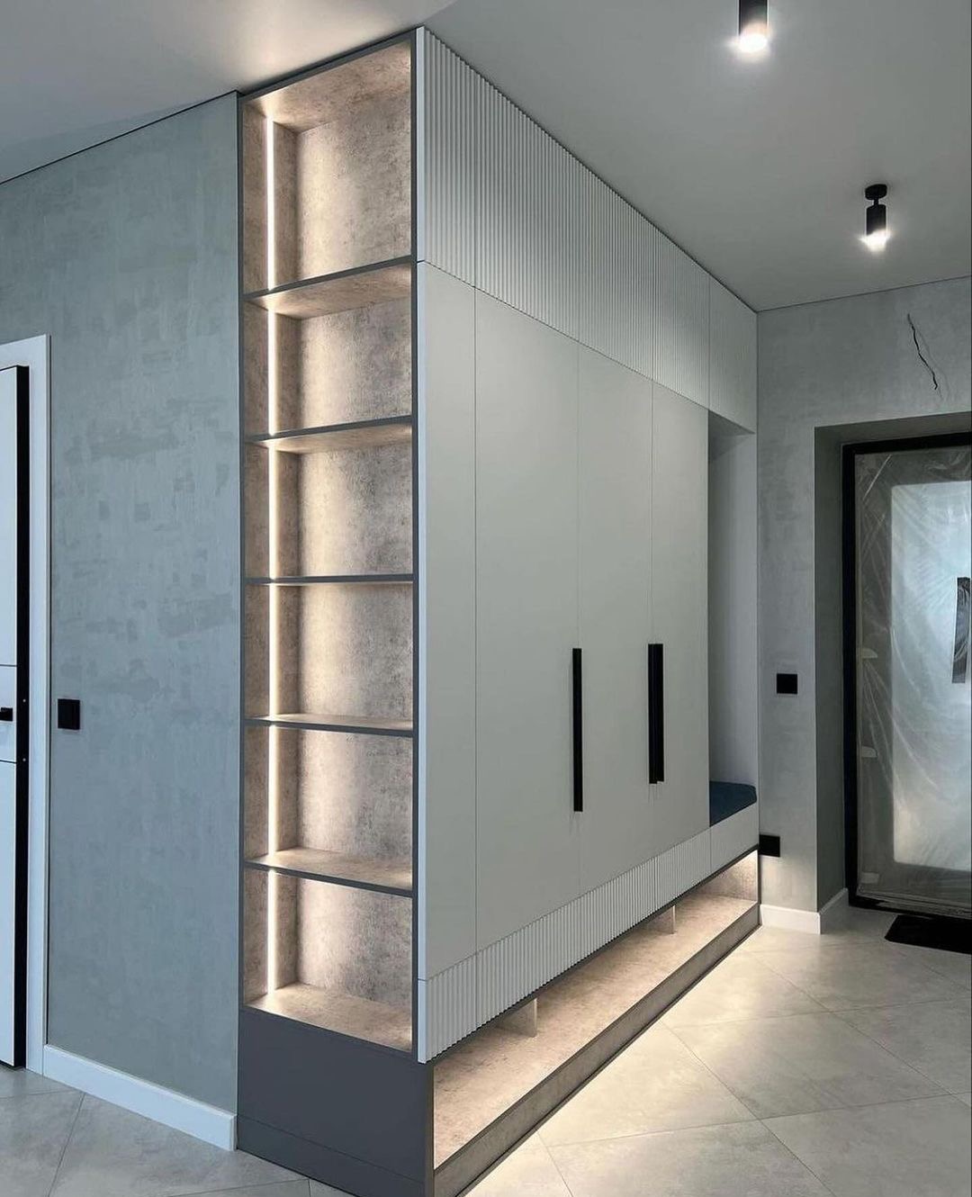 Nowoczesna zabudowa przedpokoju z szafą i otwartymi półkami podświetlonymi ledami, minimalistyczne uchwyty, szara ściana z fakturą.