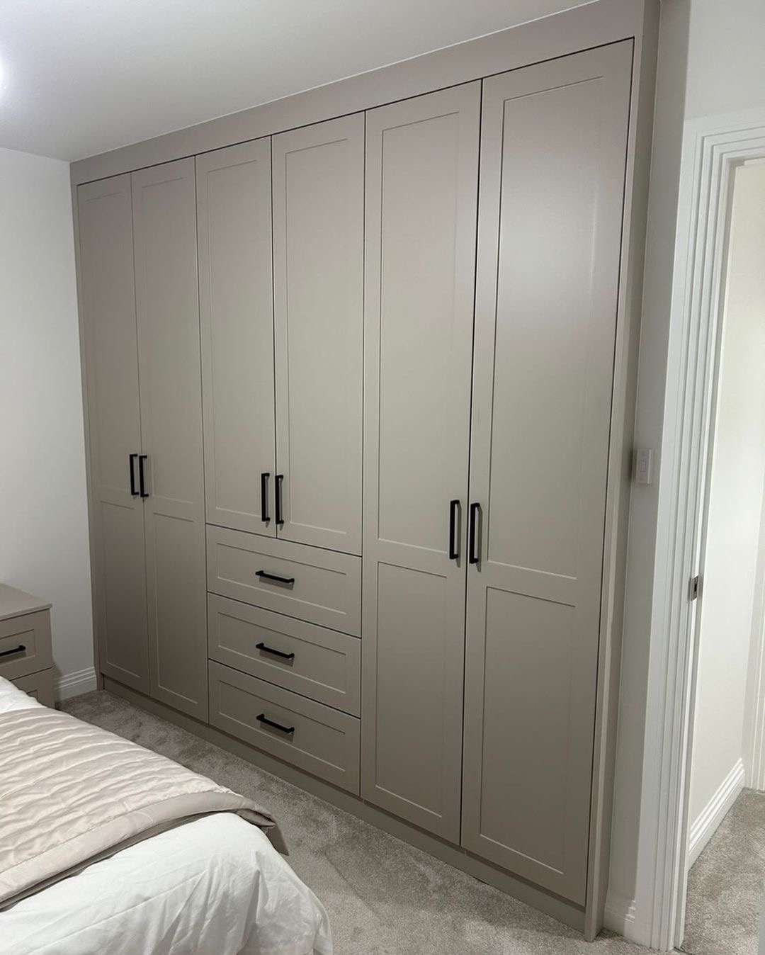 Beżowa szafa wnękowa z czarnymi uchwytami, wkomponowana w ścianę sypialni, widok z perspektywy łóżka.