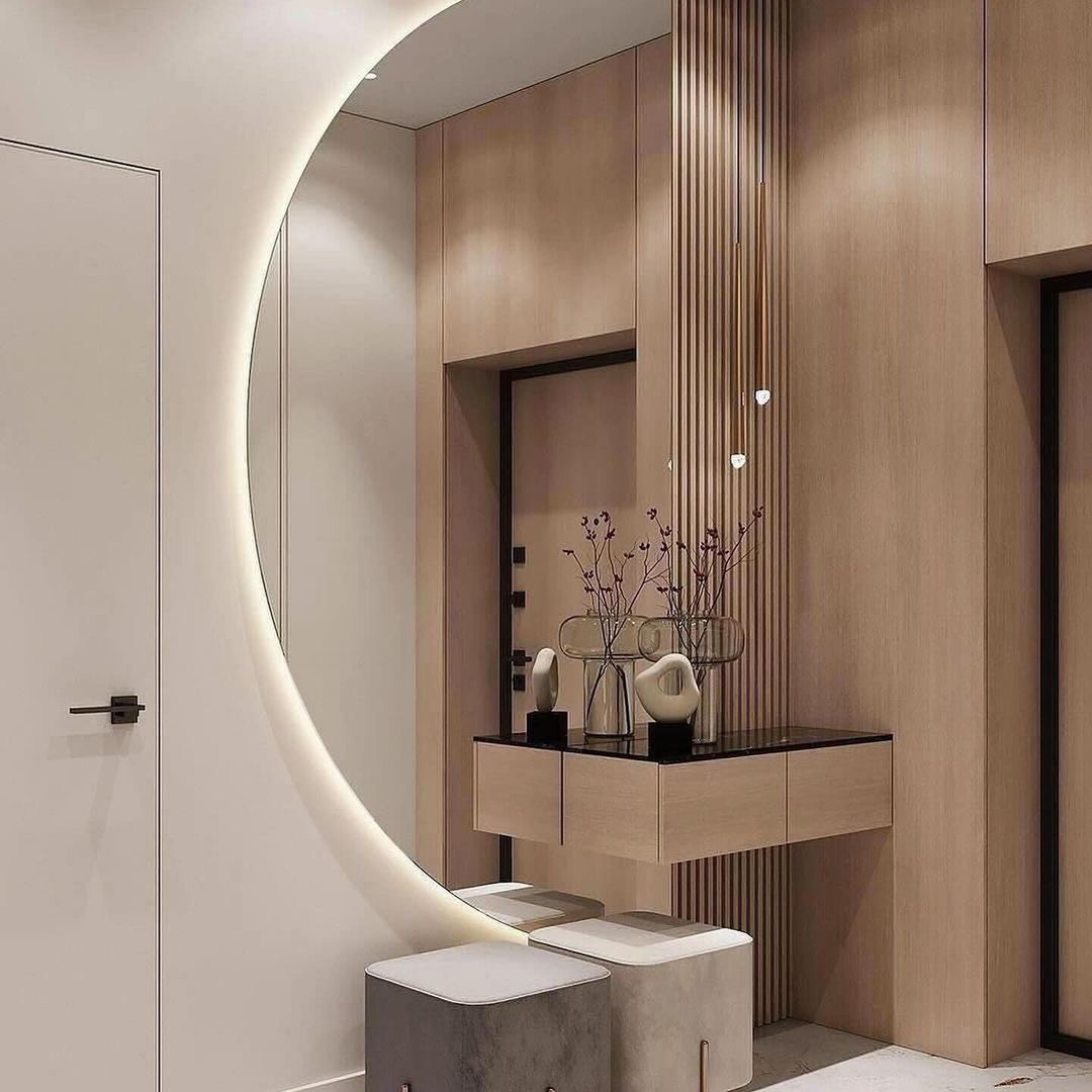 Nowoczesny przedpokój w Gdańsku z okrągłym lustrem z podświetleniem LED, drewnianymi panelami ściennymi, wiszącą konsolą z czarnym blatem i dekoracyjnymi wazonami oraz dwoma pufami w odcieniach...