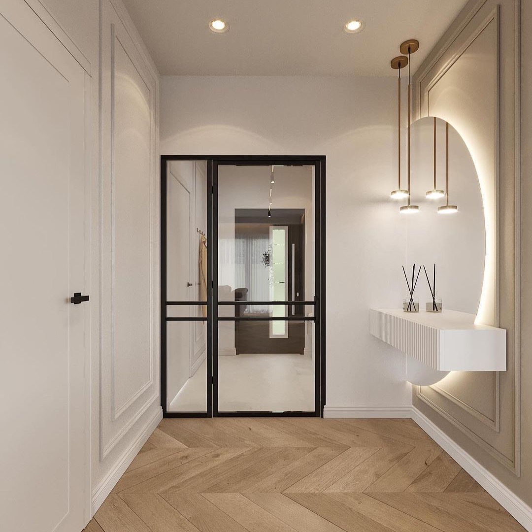 Nowoczesny przedpokój z drewnianą podłogą w jodełkę, przeszklonymi drzwiami z czarnymi szprosami, białymi szafami w zabudowie, konsolą z oświetleniem LED i wiszącymi lampami w kolorze złotym.