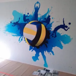 Ściana w Pruszkowie ozdobiona malunkiem przedstawiającym piłkę do siatkówki i sylwetki siatkarzy na tle niebieskich plam, zabezpieczona podłoga z widocznymi materiałami informacyjnymi.