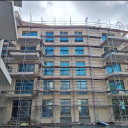 Bartosz Doszko... - Budynek wielorodzinny w trakcie remontu elewacji, okna zabezpieczone folią, widoczne rusztowania.