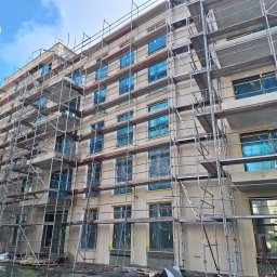 Bartosz Doszko... - Budynek w trakcie prac elewacyjnych, okna zabezpieczone folią, rusztowania na całej fasadzie, widok z dołu na kilka pięter.