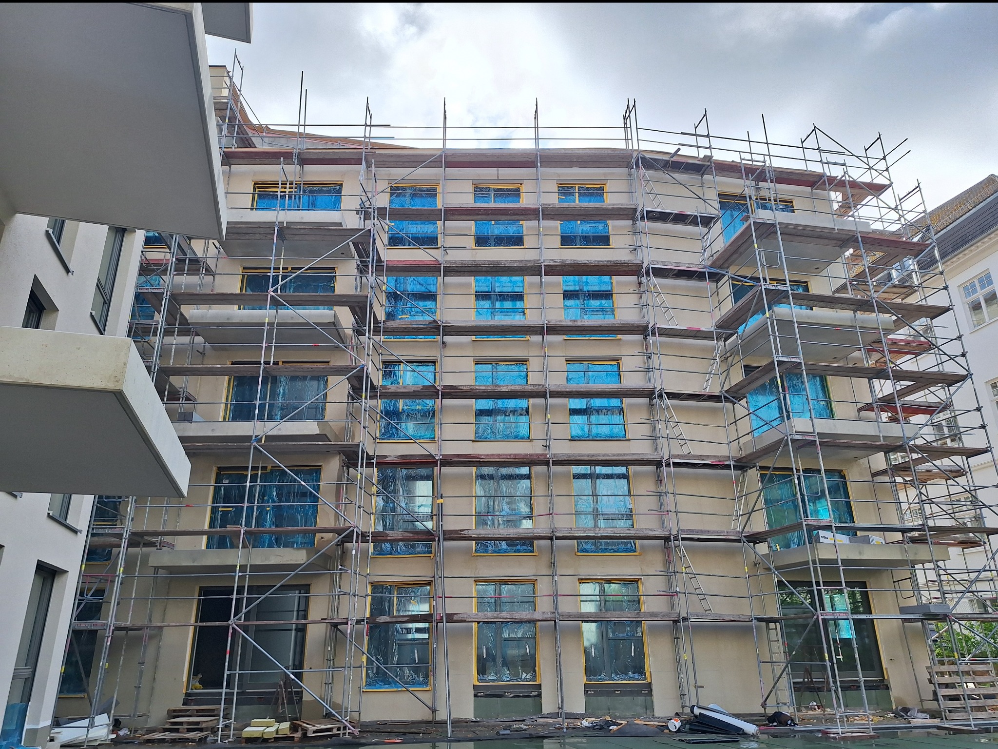 Budynek wielorodzinny w trakcie remontu elewacji, okna zabezpieczone folią, widoczne rusztowania.