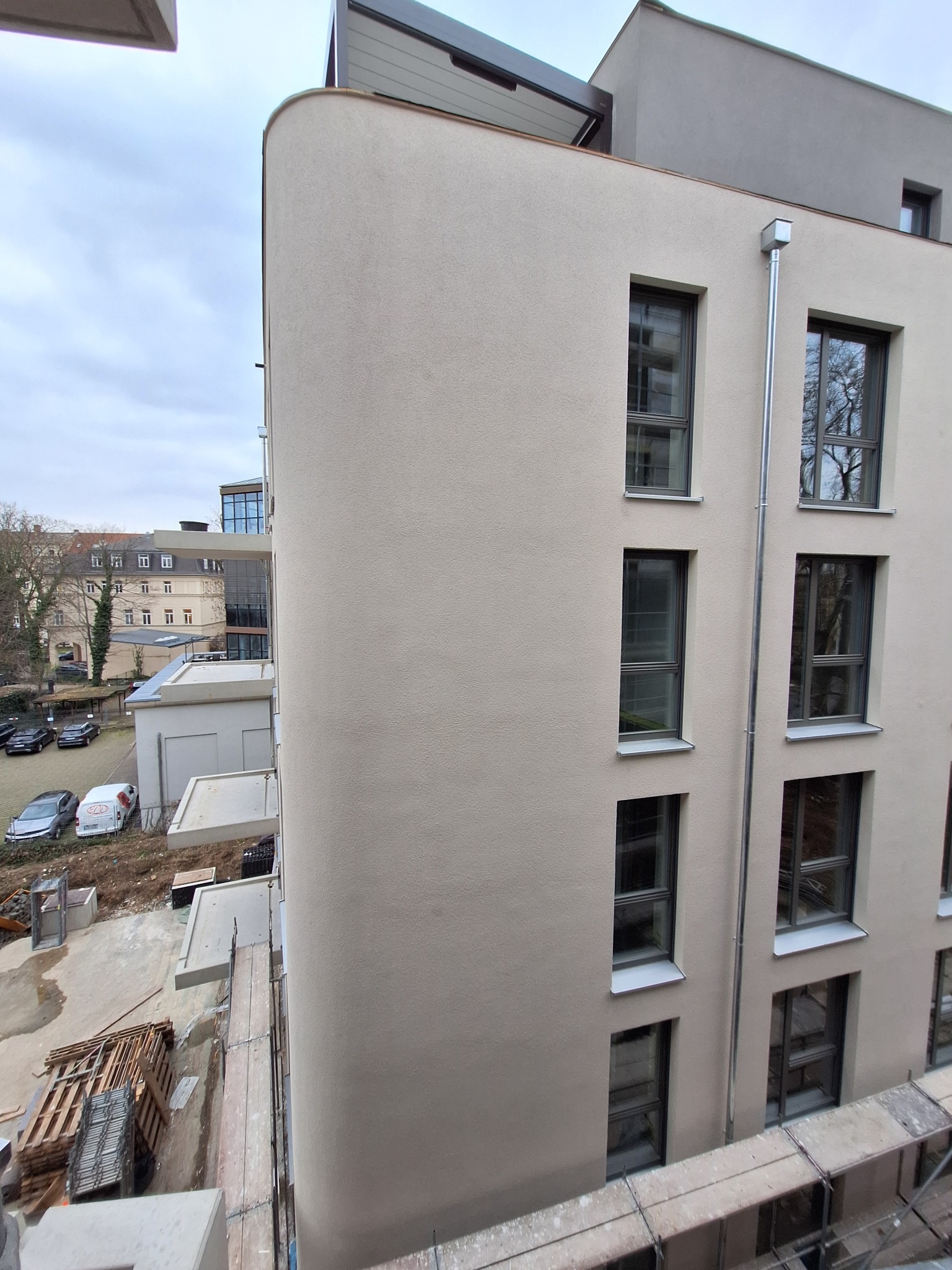 Fragment elewacji budynku wielorodzinnego w trakcie budowy, z widocznymi oknami i rusztowaniem, na tle pochmurnego nieba.