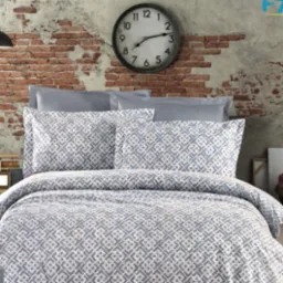 Gotowa pościel w geometryczny wzór na łóżku, szare poduszki, ceglana ściana w tle i duży zegar.