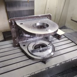 LEGAL & TECHNICAL SUPPORT CENTRE SPÓŁKA Z OGRANICZONĄ ODPOWIEDZIALNOŚCIĄ - Metalowy element z otworami, obrabiany na frezarce CNC, widoczne wióry i chłodziwo.