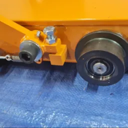 Pomarańczowa konstrukcja stalowa z elementami mocującymi, śrubami i sprężyną, wykonana w Piotrowicach. Widoczne detale połączeń i wykończenia.