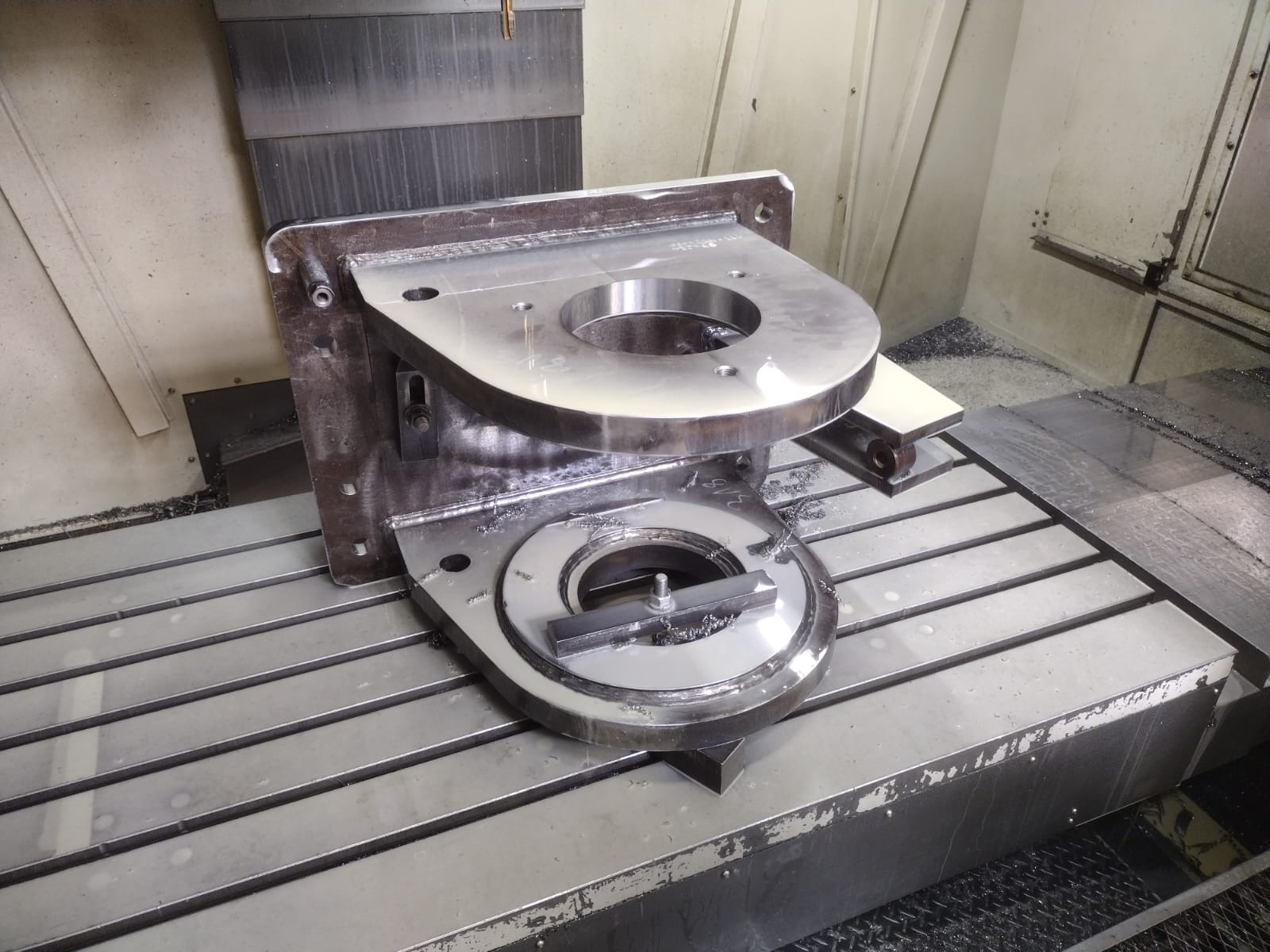 Metalowy element z otworami, obrabiany na frezarce CNC, widoczne wióry i chłodziwo.