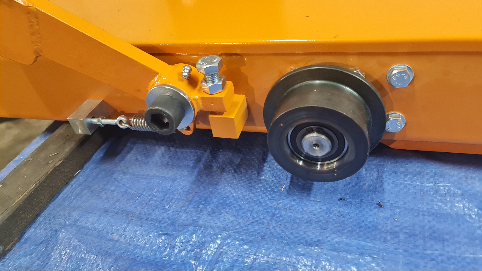 Pomarańczowa konstrukcja stalowa z elementami mocującymi, śrubami i sprężyną, wykonana w Piotrowicach. Widoczne detale połączeń i wykończenia.