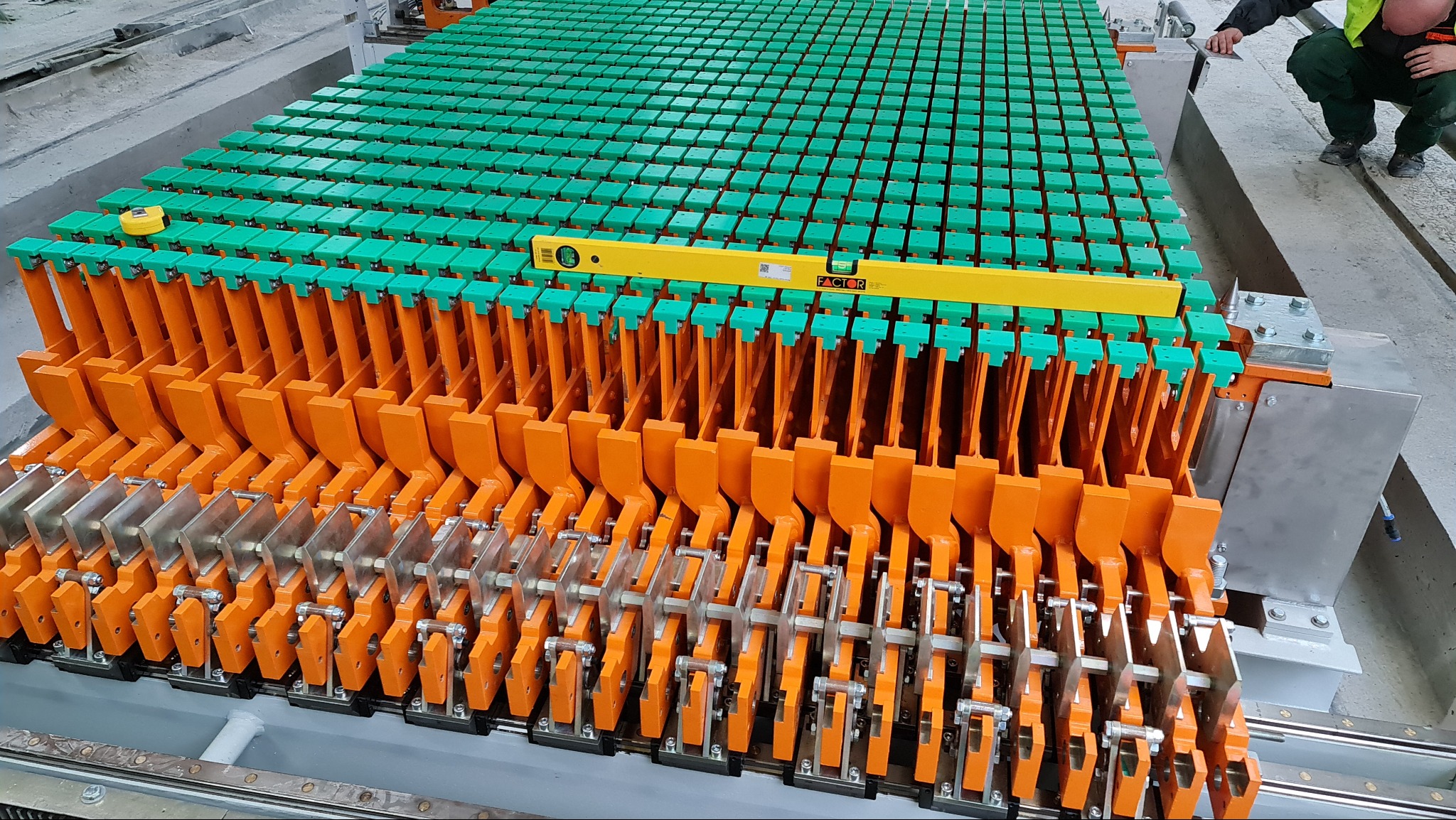 Szczegółowe ujęcie formy do prefabrykatów betonowych z elementami pomalowanymi na pomarańczowo i zielono, sprawdzanej poziomicą, z widocznym fragmentem osoby w prawym górnym rogu.