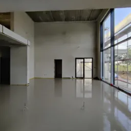 Świeżo wylana, gładka wylewka anhydrytowa w przestronnym, surowym wnętrzu z dużymi oknami i widocznymi elementami konstrukcyjnymi sufitu; widoczne narzędzia do rozprowadzania wylewki.