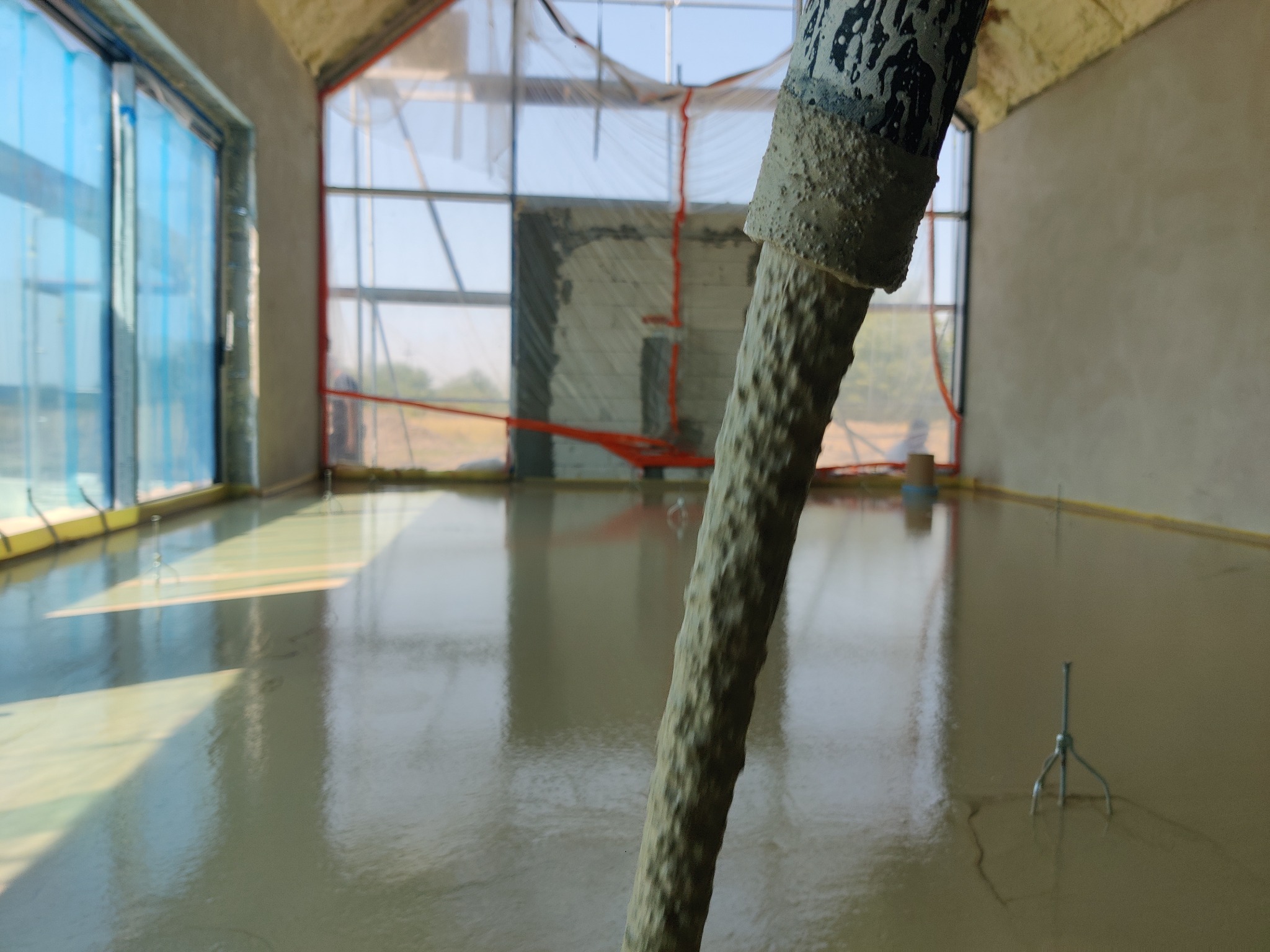 Wylewka samopoziomująca rozprowadzana w nowym budynku z dużymi oknami, widoczne narzędzie do rozprowadzania masy.