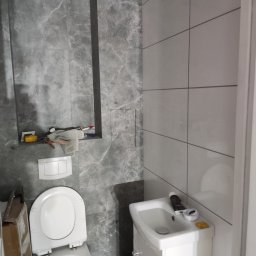 VS Wykończenie wnętrz Viktor Semenov - Łazienka w trakcie wykańczania: biała umywalka z szafką, toaleta oraz szare płytki imitujące marmur na ścianach, widoczne narzędzia i materiały budowlane.