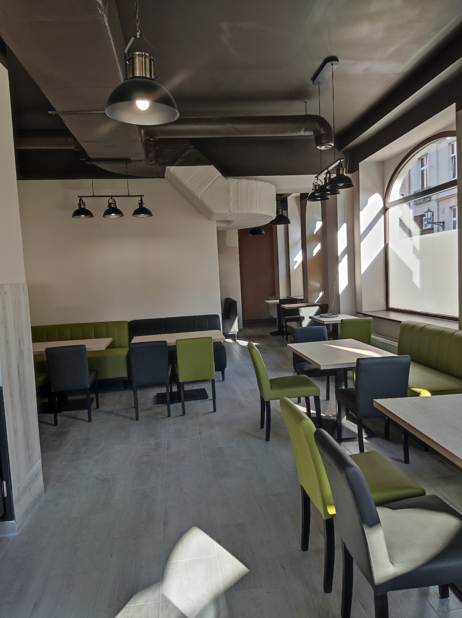 Wnętrze biura z nowoczesnym oświetleniem, szarymi krzesłami i zielonymi sofami, widok na okno z zewnątrz.