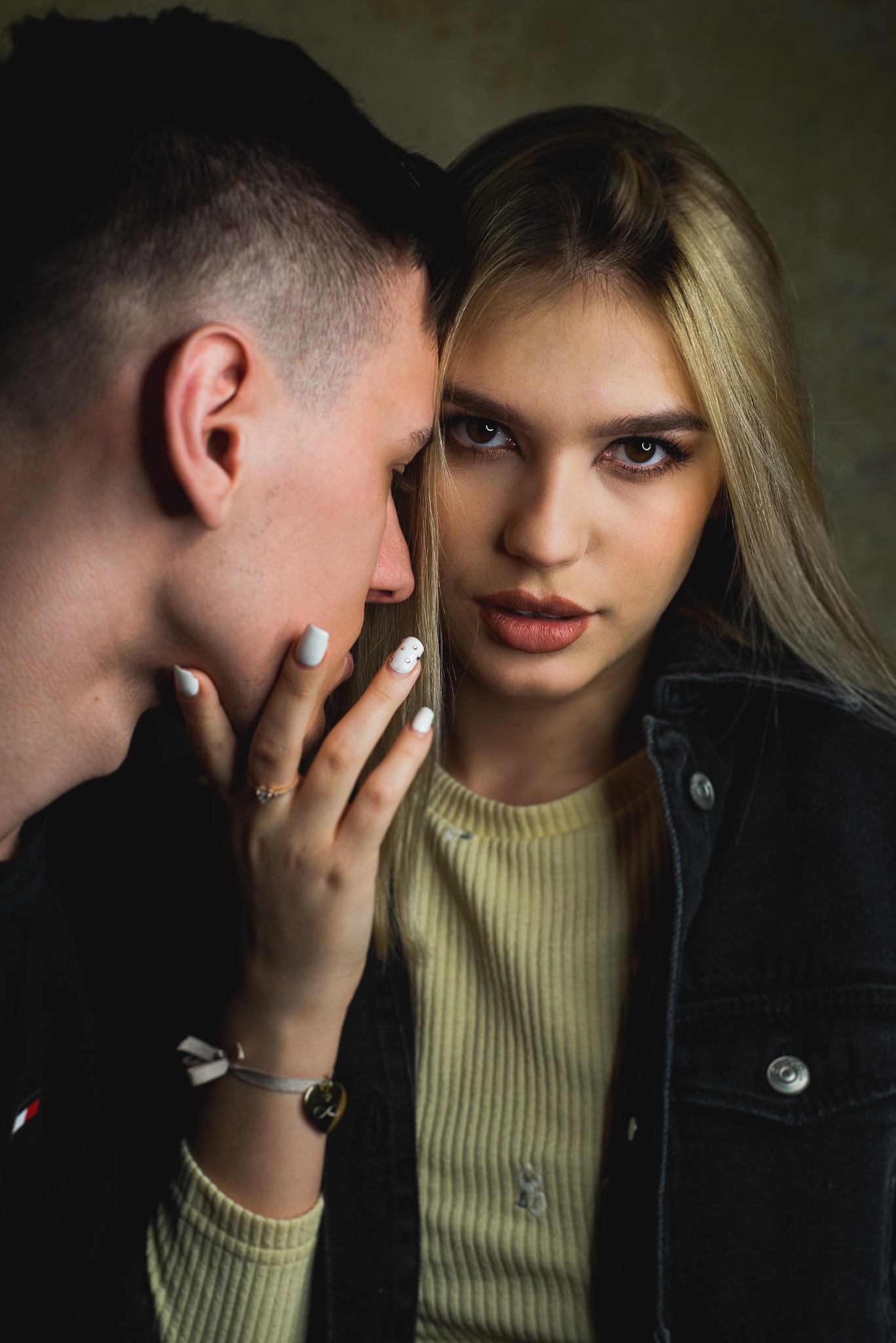 Portret zbliżeniowy młodej kobiety z blond pasemkami, spoglądającej w obiektyw, z ręką ozdobioną pierścionkiem i bransoletką dotykającą twarzy mężczyzny z krótkimi włosami