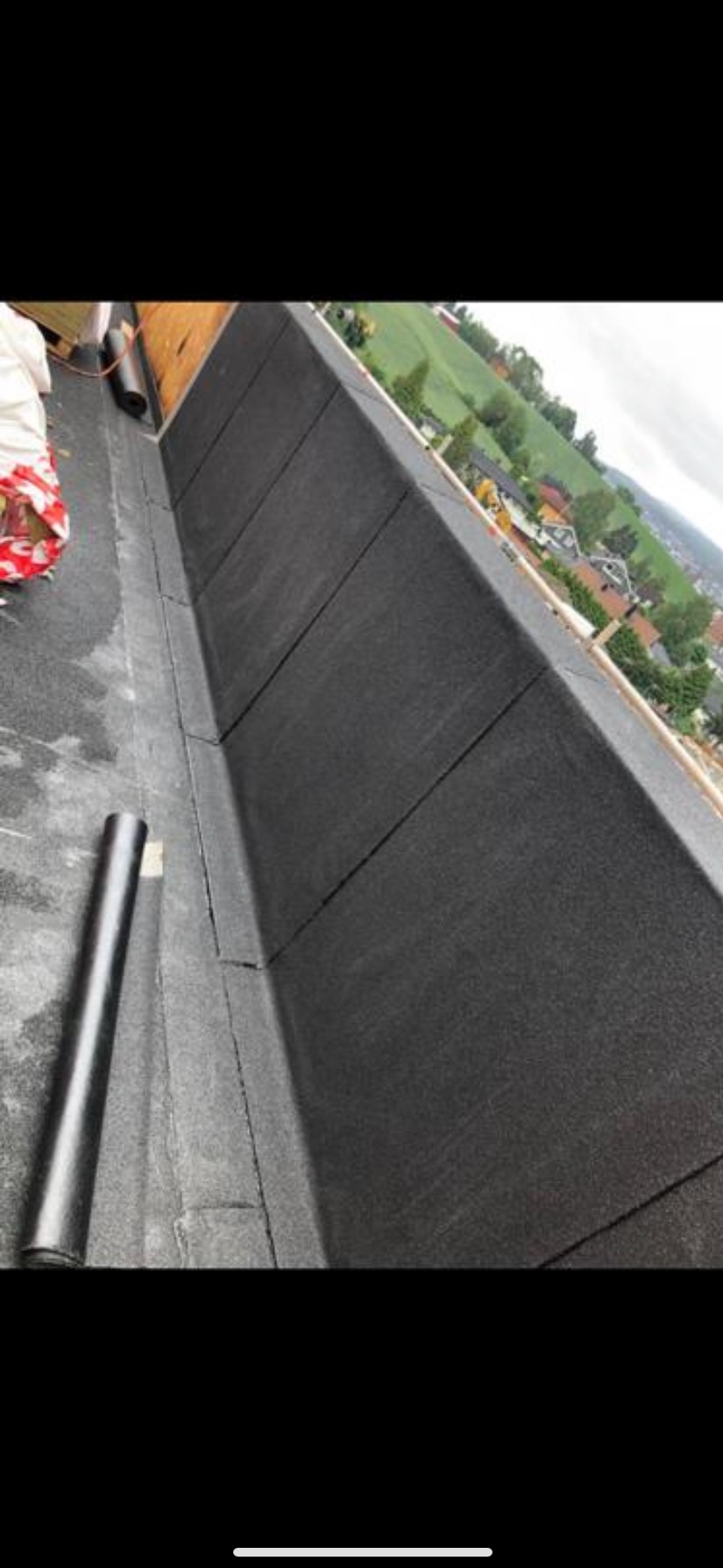 Fragment dachu pokrytego papą termozgrzewalną z widoczną rolką papy i fragmentem krajobrazu w tle.