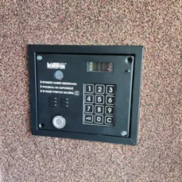 Panel domofonu Laskomex CD-2502 z klawiaturą numeryczną i wyświetlaczem LED, zamontowany na ścianie o chropowatej fakturze.