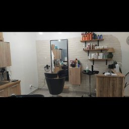 M-W Invest - Wnętrze salonu z fotelem fryzjerskim, umywalką i drewnianymi półkami na kosmetyki, wykończone cegłą dekoracyjną.