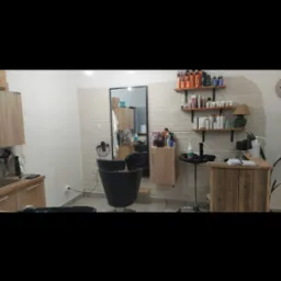 Wnętrze salonu z fotelem fryzjerskim, umywalką i drewnianymi półkami na kosmetyki, wykończone cegłą dekoracyjną.